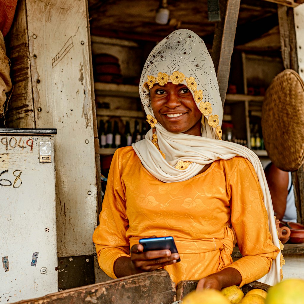 Photo of a smiling shopkeeper at her market stall holding a phone while customer messages get instant replies