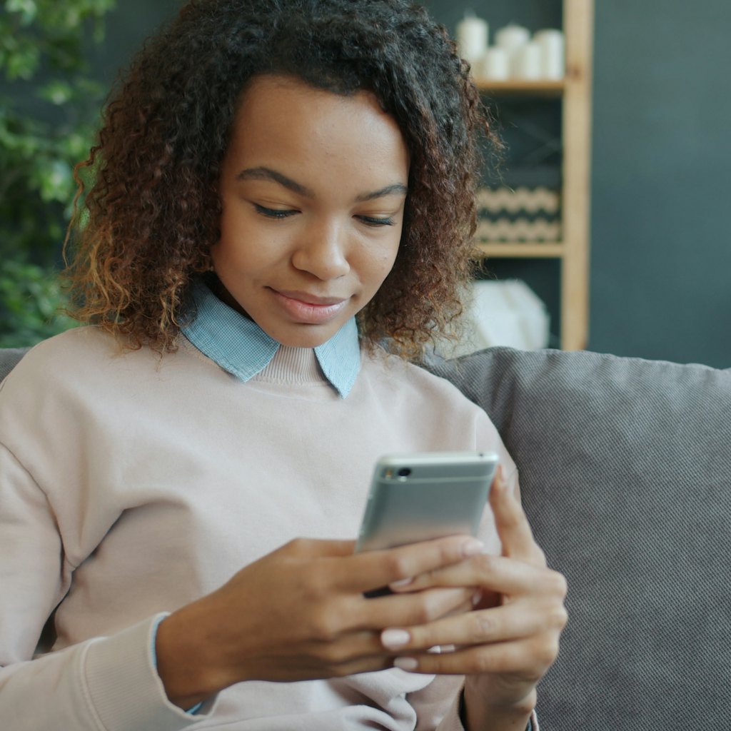 Photo of a woman on a sofa looking down at her phone as she texts